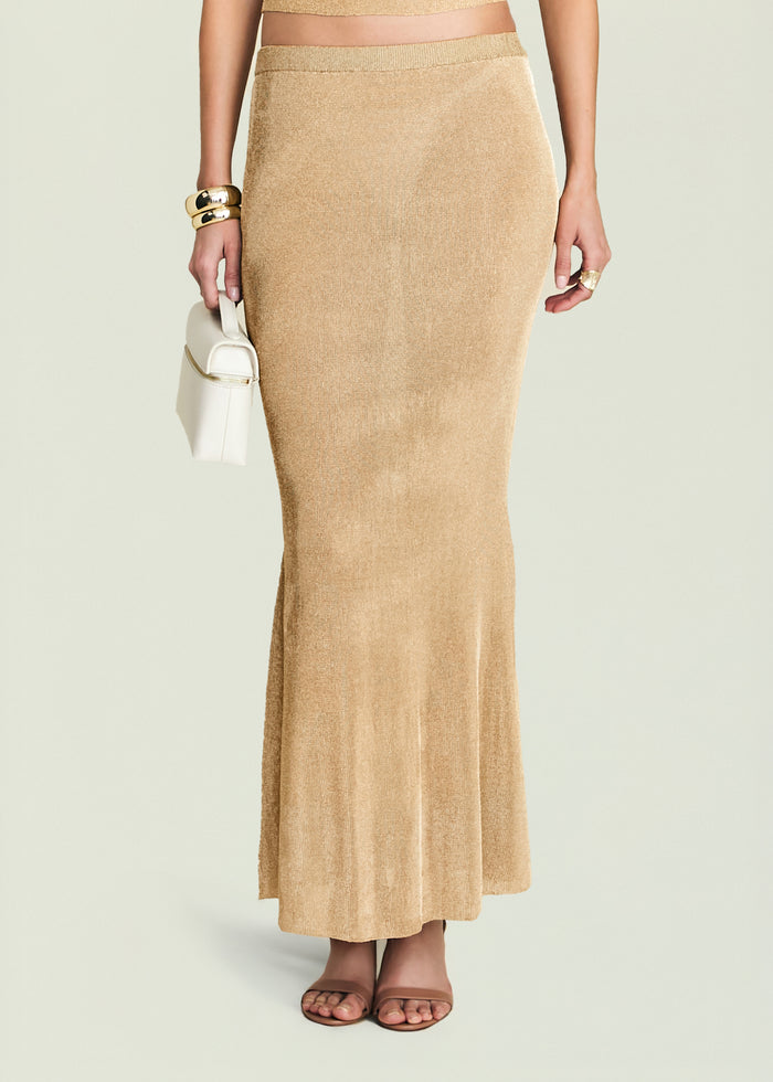 Harmony Metallic Knit Skirt worn by a model paired with a white mini bag and chunky gold bracelets.