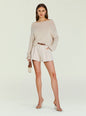Model wearing beige Serafina Sweater off the shoulder with cream shorts, brown belt, nude heels and a small handbag. thumbnail image 2 of 5