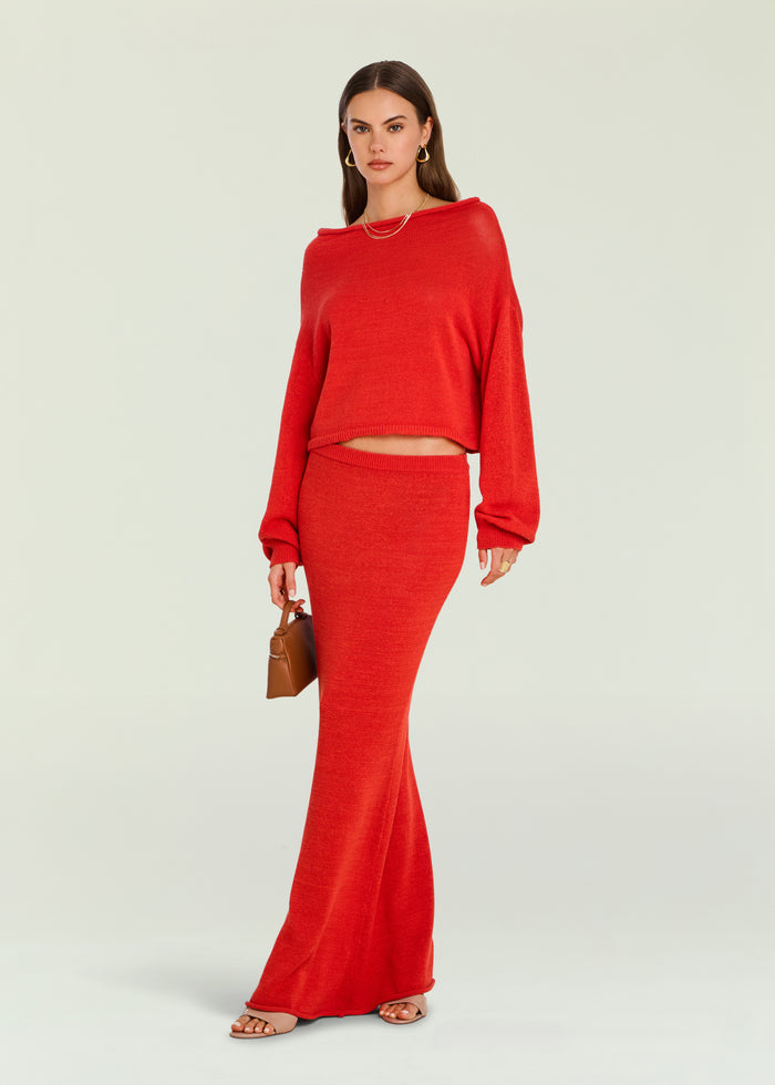 Full length shot of a model wearing a red cropped knit sweater and matching red skirt, holding a brown handbag