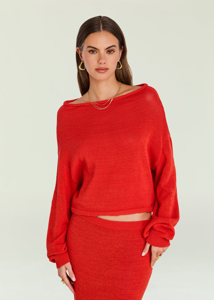Model wearing bright red Serafina Sweater with a wide boat neckline and relaxed fit, gold earrings visible.