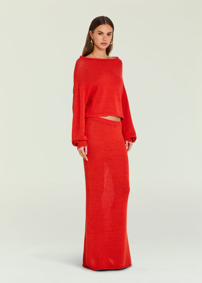 Full-length shot of a model wearing red Serafina Sweater with matching floor-length knit skirt against a pale backdrop.