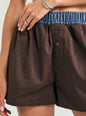 Close-up of a person wearing brown shorts with a blue patterned elastic waistband and front buttons, against a light neutral background. thumbnail image 3 of 5