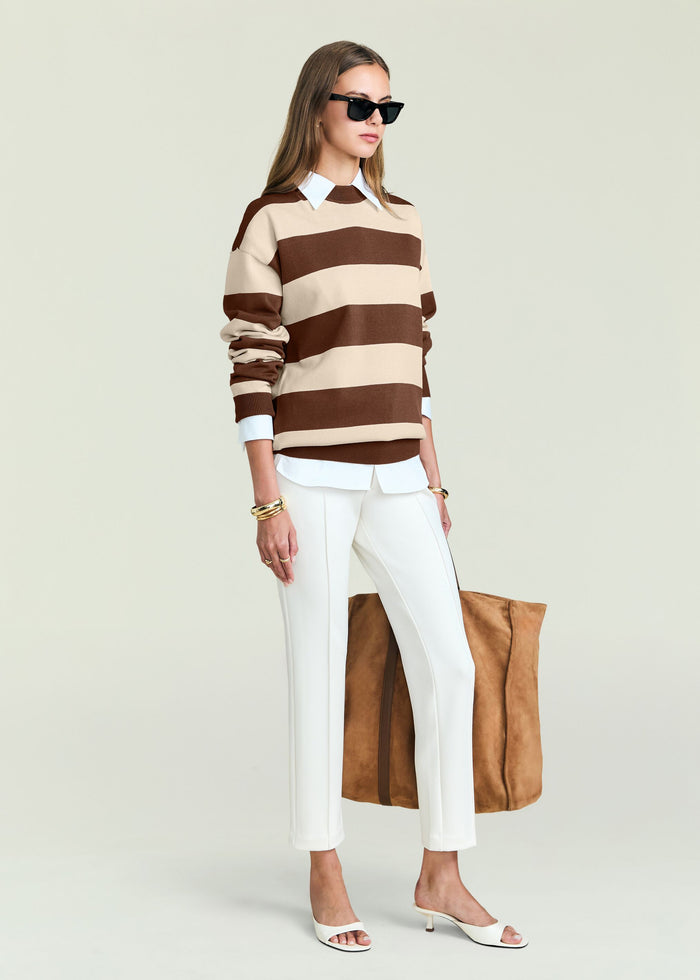Model wearing Bryn Knit Sweater with wide brown and beige stripes over a white shirt, white trousers, and sunglasses.