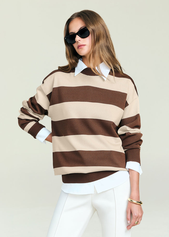 Woman in an oversized beige and brown striped knit sweater with white shirt underneath and sunglasses