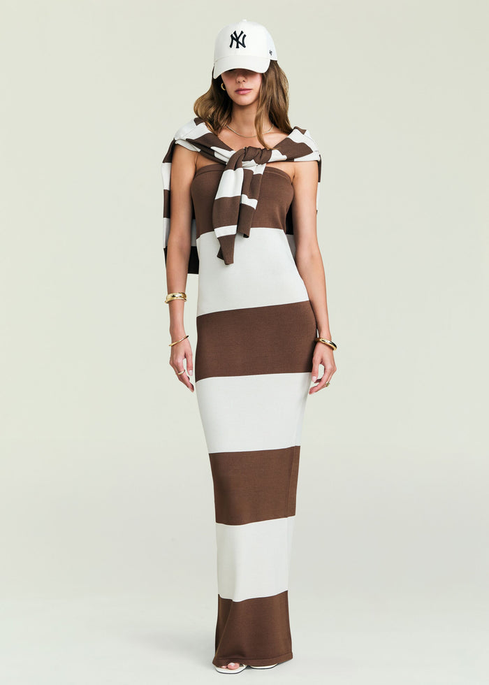 Model facing forward in a brown and cream striped knit maxi dress with a white collar shirt and white baseball cap
