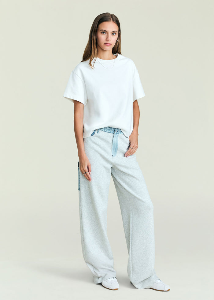 Front view of a model wearing Travis Denim Pant in light gray with a denim waist belt and a white oversized T shirt.