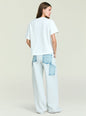 Back view of a model in Travis Denim Pant with large blue denim patch pockets against a pale backdrop. thumbnail image 4 of 5