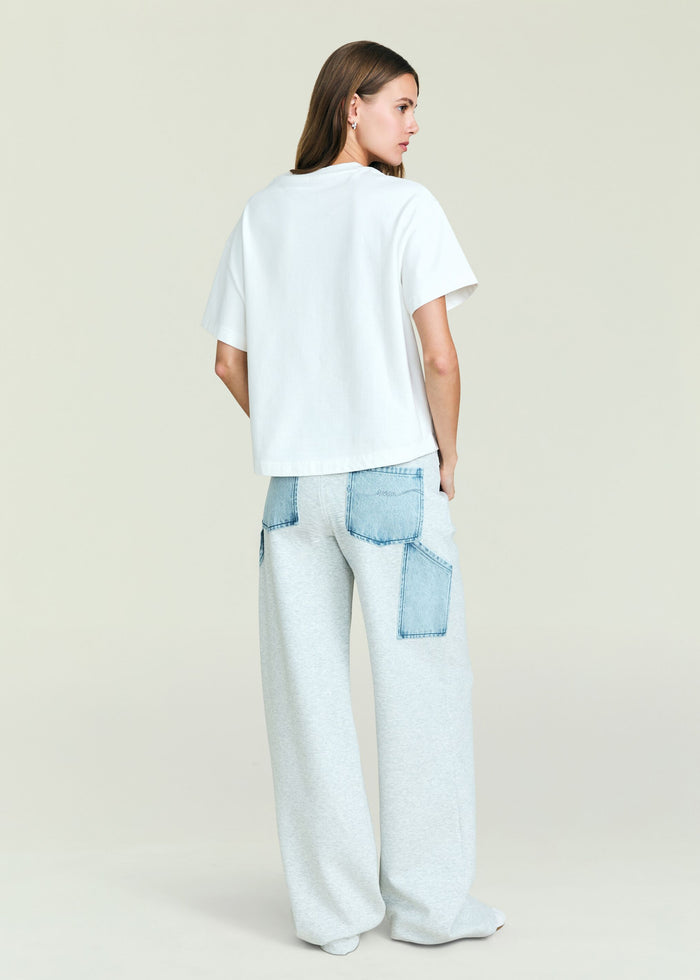 Back view of a model in Travis Denim Pant with large blue denim patch pockets against a pale backdrop.