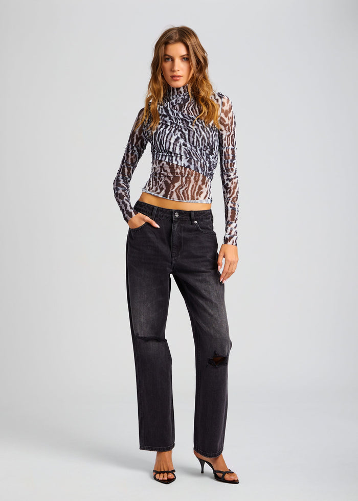 Front three quarter view of a model in a zebra print sheer wrap top with distressed black jeans and sandals