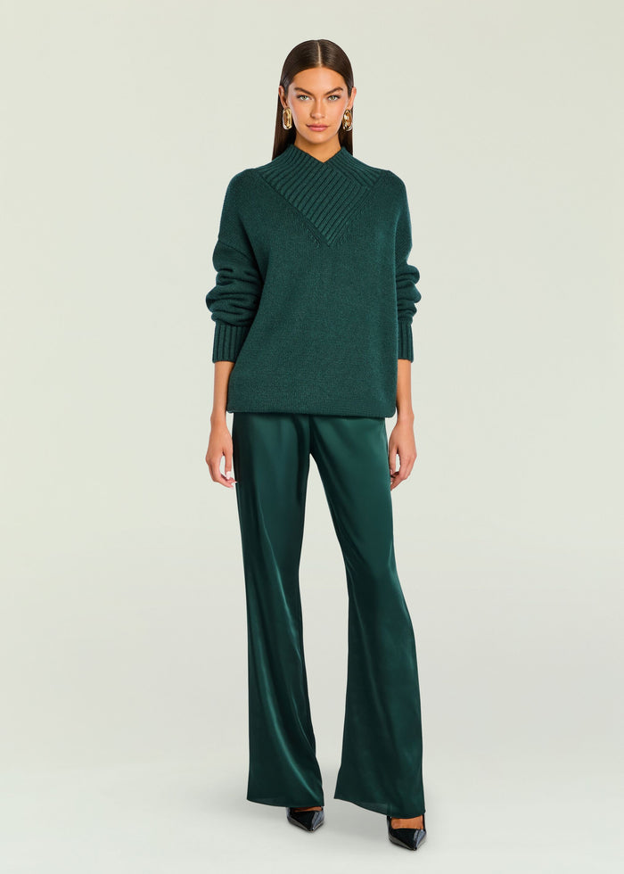 Front view of model wearing emerald green knit sweater and satin pants with gold earrings and black heels