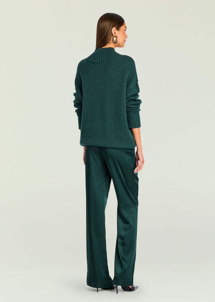 Back view of model in emerald green knit sweater and matching satin pants with gold earrings