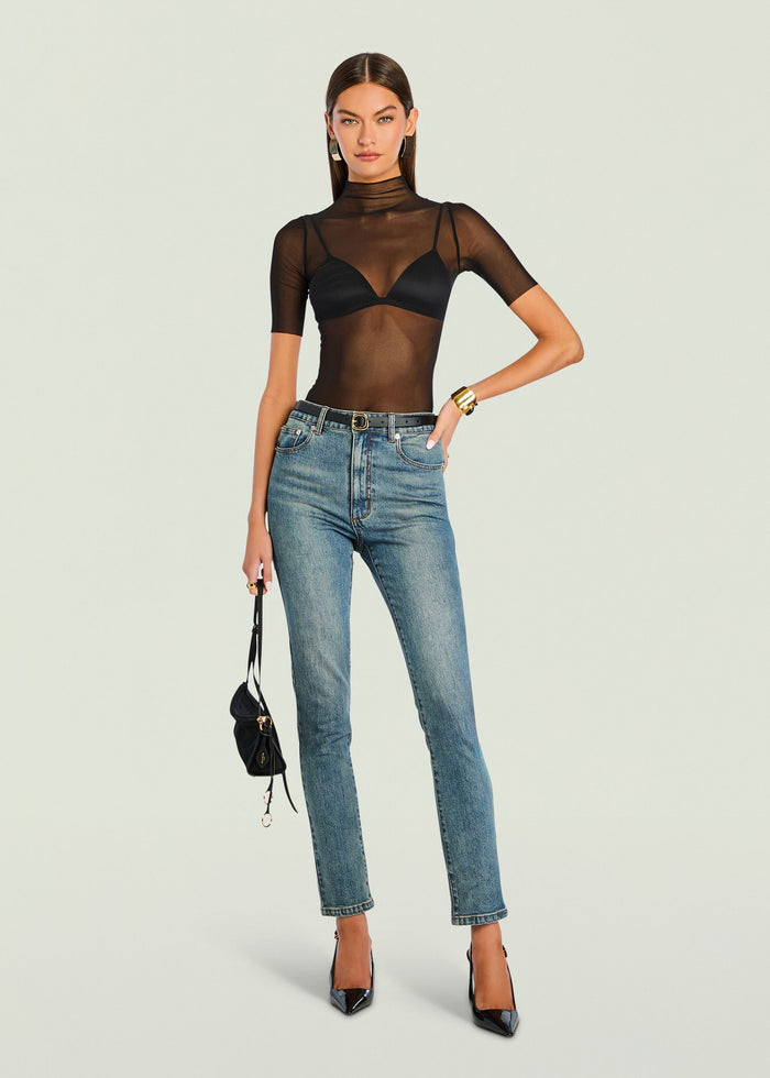 Model wearing Gail Bodysuit a black sheer mesh bodysuit over a bralette with blue jeans