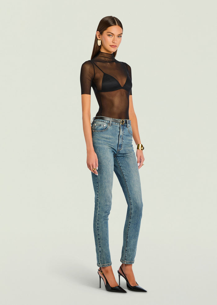 Three-quarter view of model in Gail Bodysuit sheer black top with bralette and denim jeans.