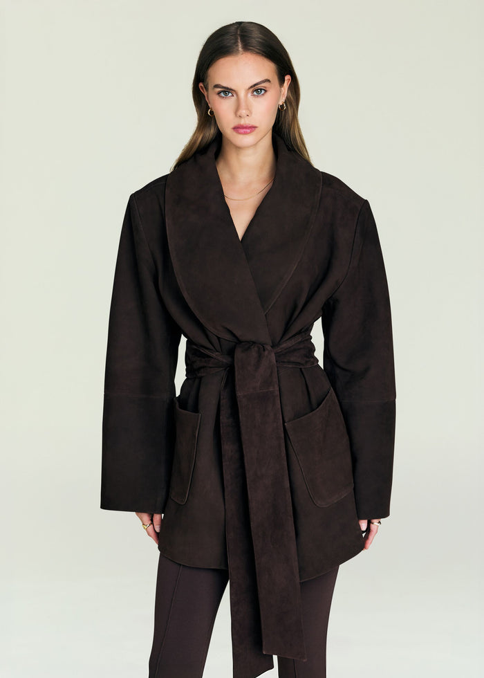 Model in a dark brown suede wrap jacket with wide lapels and a tied belt.