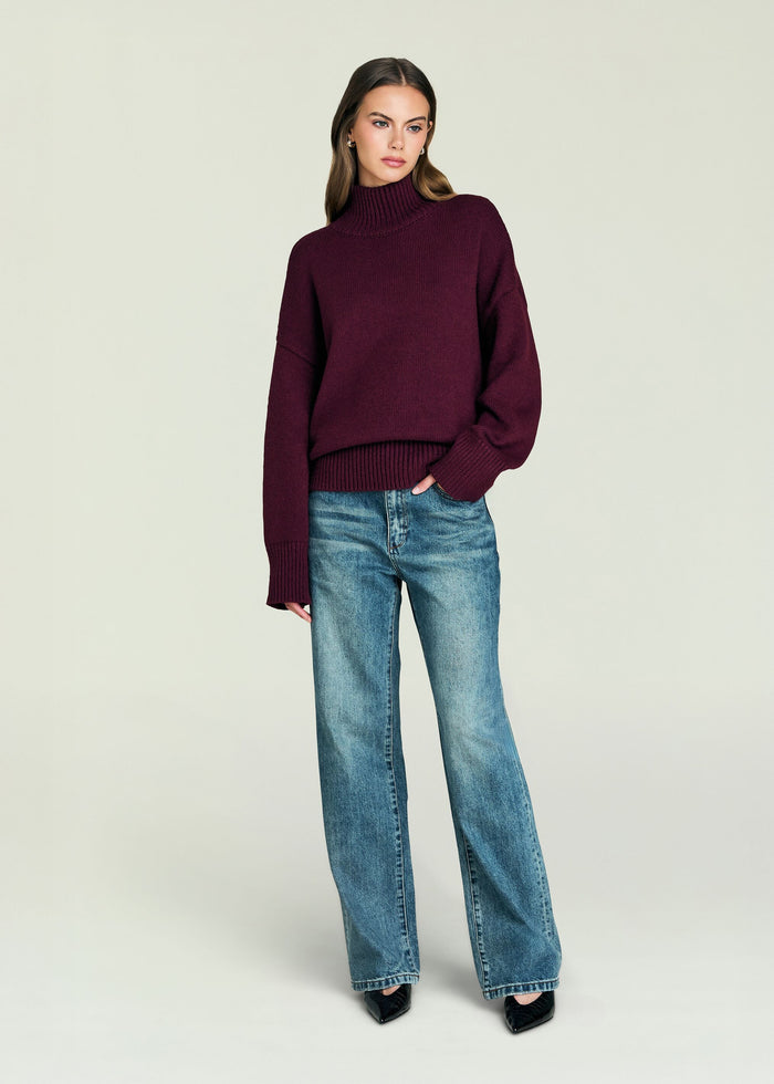 Model wearing a burgundy Elsa Turtleneck Sweater with a relaxed fit and ribbed cuffs and hem, paired with jeans.