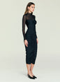 Side view of a model wearing the black Emilyn Midi Dress with sheer sleeves and ruched front. thumbnail image 3 of 5