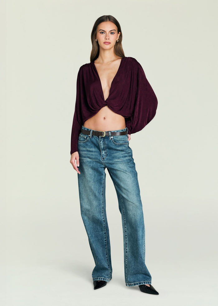 Model wearing burgundy Jerome Top with off the shoulder neckline and front twist knot, paired with denim jeans.