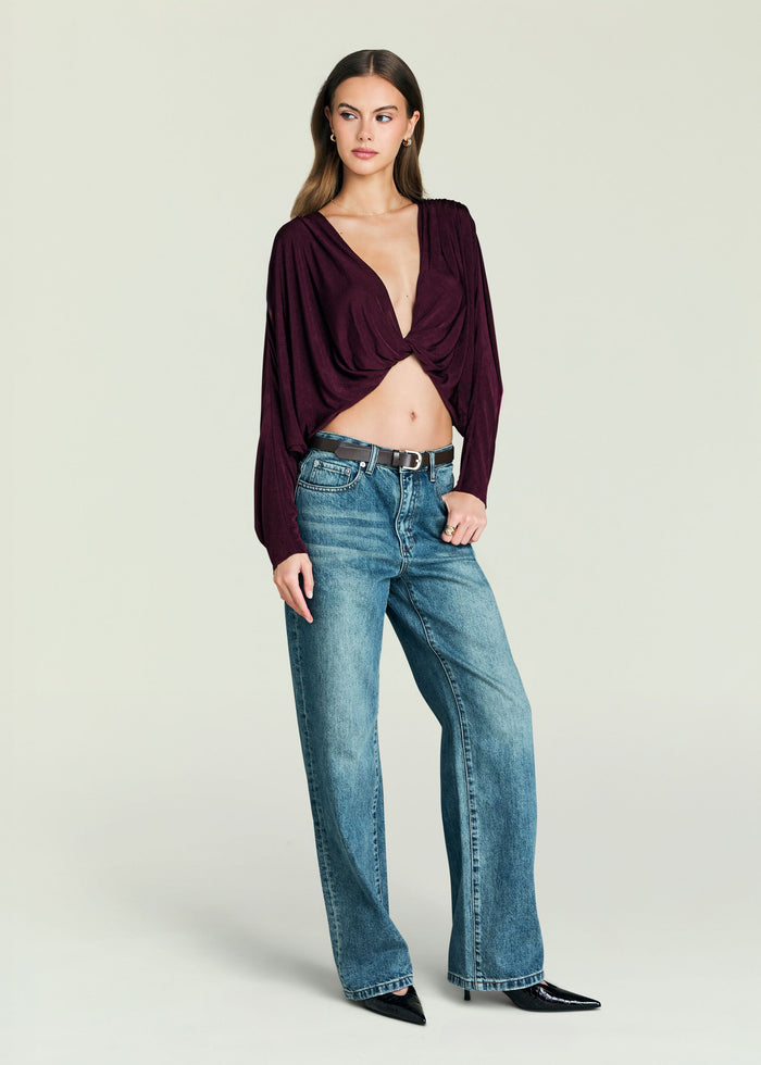 Model wearing burgundy Jerome Top with twisted front knot and long sleeves, paired with blue jeans.