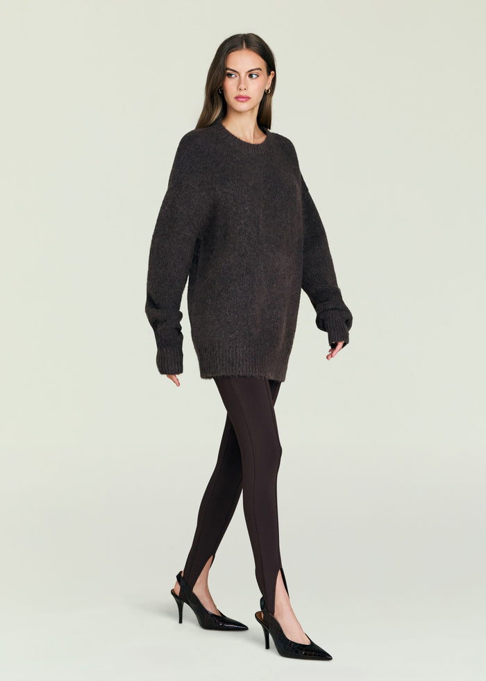 Model wearing a dark oversized knit sweater with a crew neck against a pale backdrop.