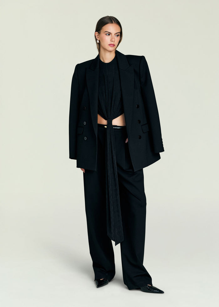 Model wearing a black Laura Top tied at the waist under an oversized black blazer with matching trousers