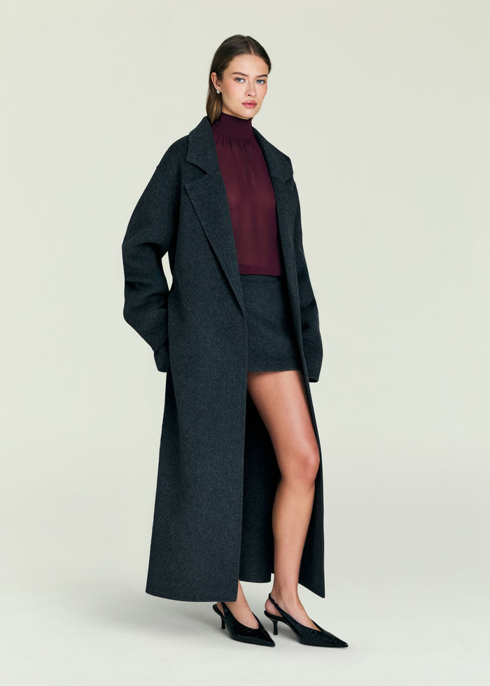 Model wearing a charcoal Lyli Wool Coat over a burgundy top and matching skirt photographed from a side angle