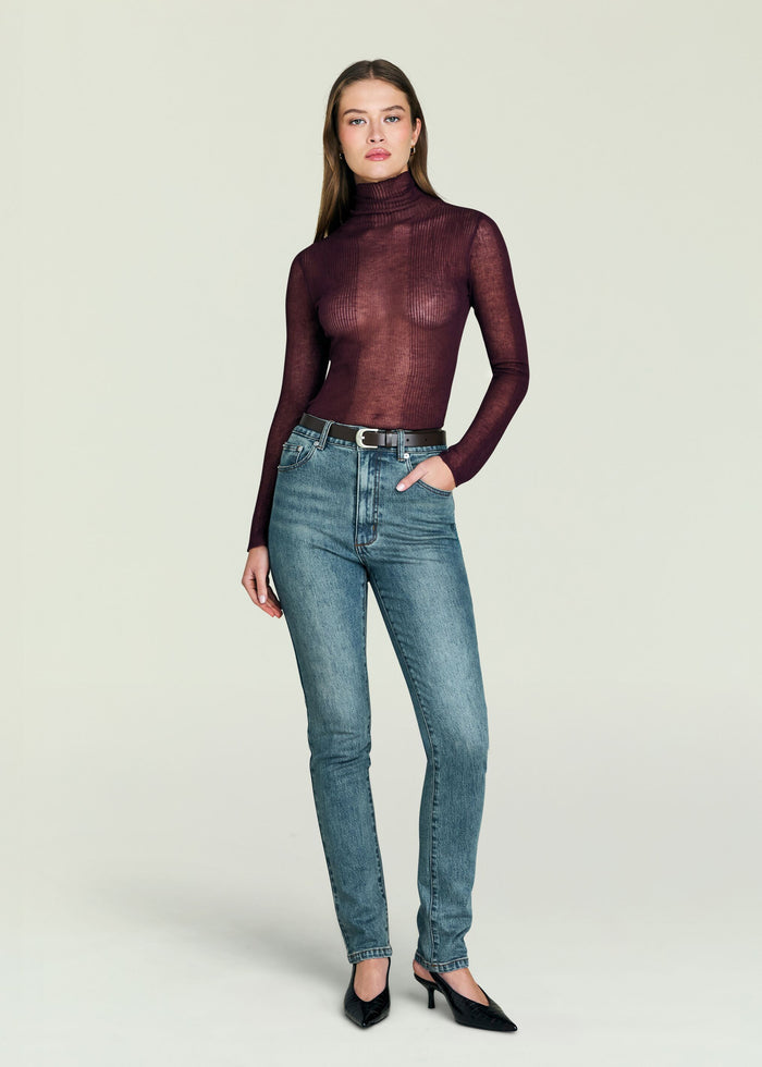 Model wearing Celia High Rise Skinny Jeans in light wash denim with a burgundy sheer turtleneck and belt.