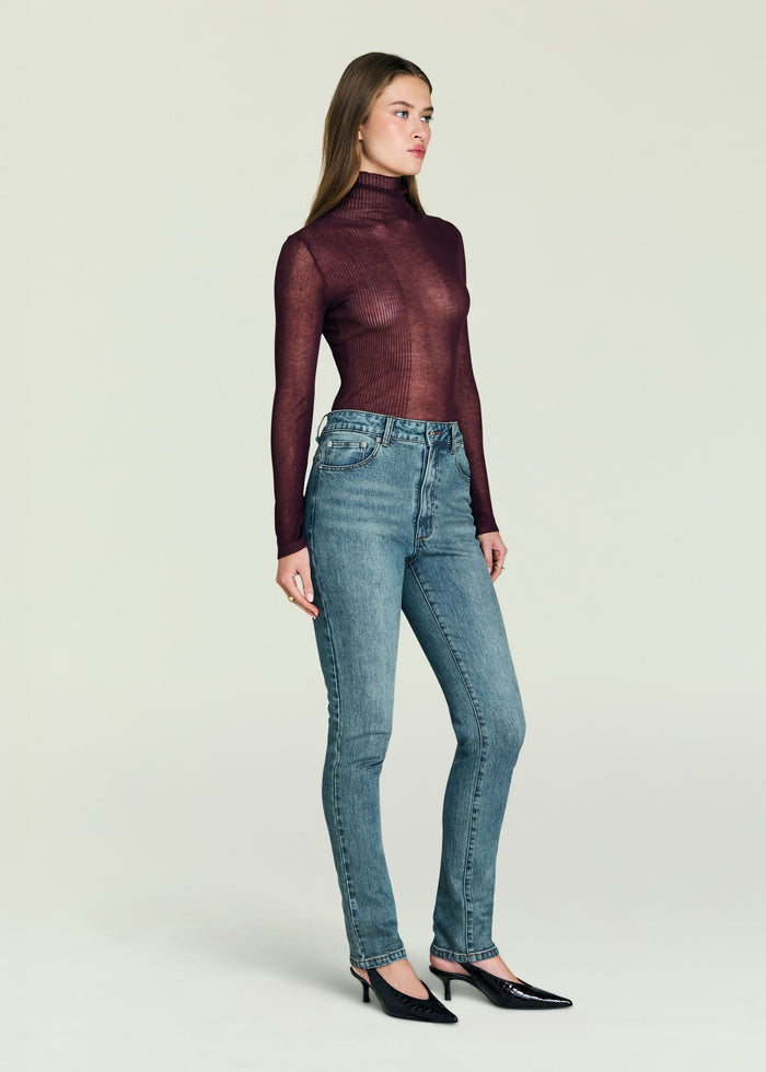 Side profile of a model wearing Celia high rise skinny jeans with a burgundy sheer turtleneck