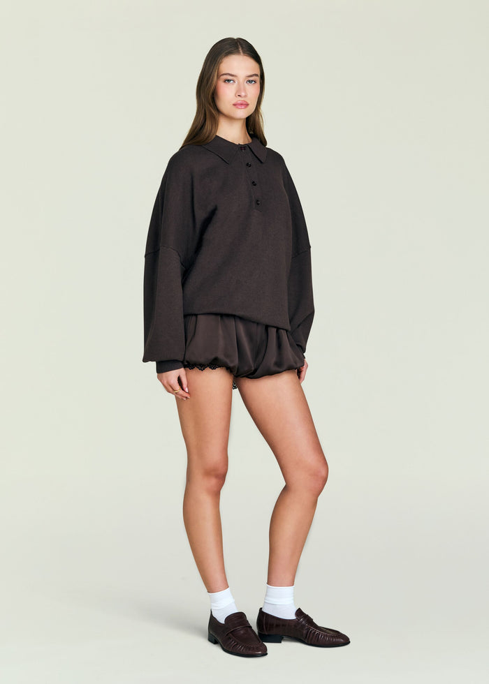 Vespen Sweater paired with satin shorts dark knit model wearing white socks and brown loafers against a pale backdrop