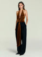Front view of a model in a copper velvet halter bodysuit with a deep plunging neckline and waist tie, paired with black wide-leg pants. thumbnail image 5 of 5