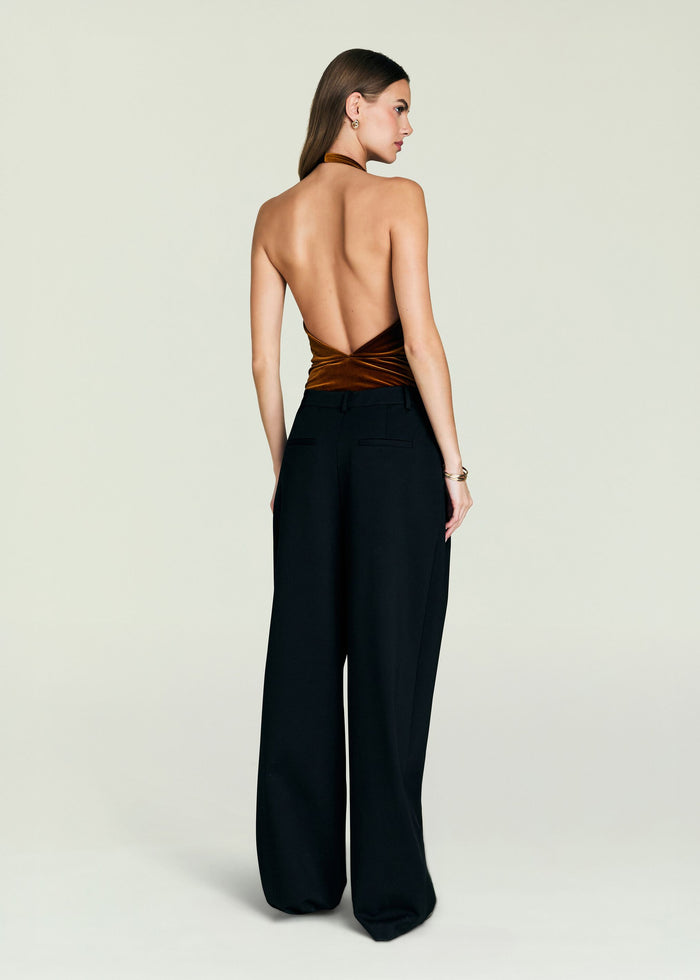 Back view of a model in a copper velvet halter bodysuit tied at the waist with black wide-leg pants.