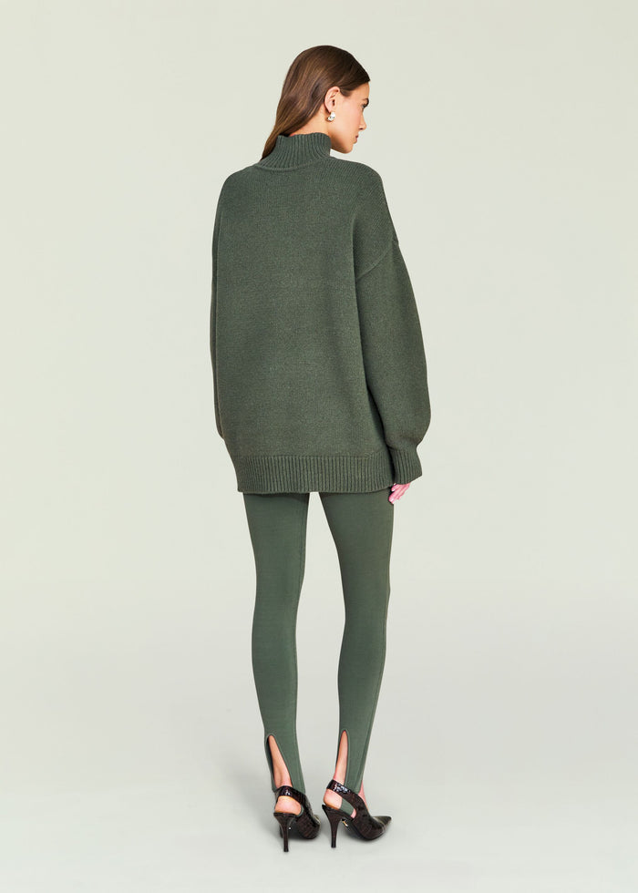 Back view of model wearing olive green Kelsey Stirrup Leggings and an oversized sweater