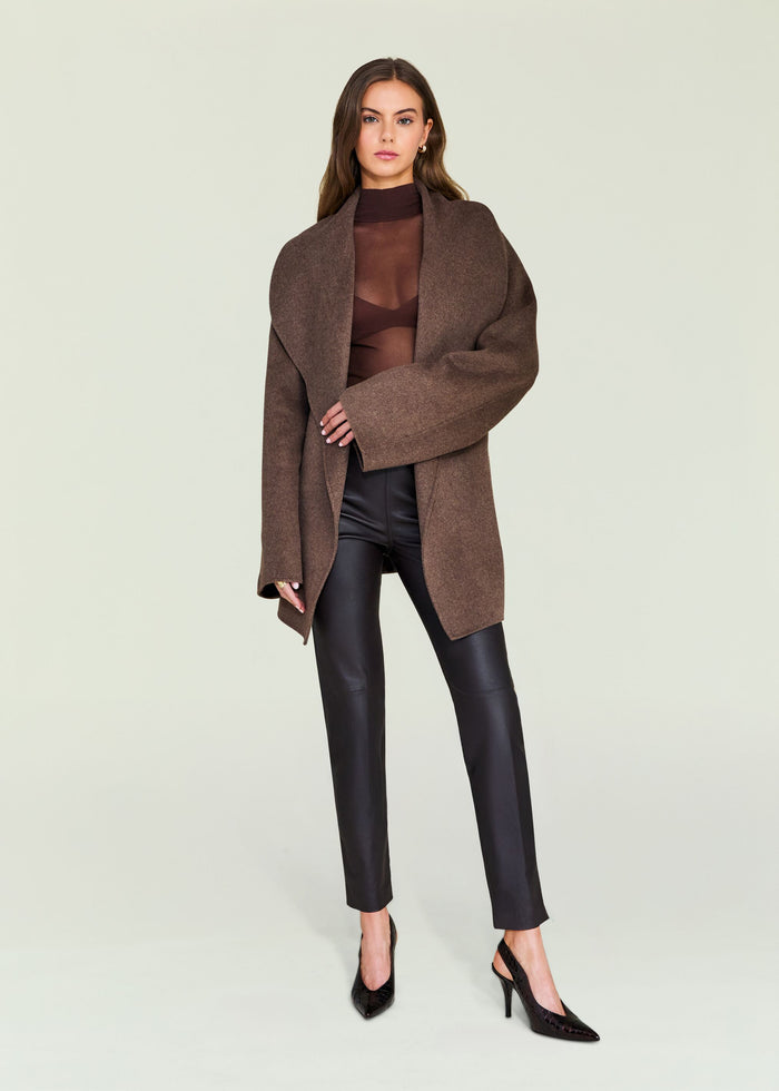 Model wearing Cyra Leather Legging with a brown oversized coat in a studio.