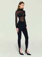 Front view of a model in a black sheer top over a black bra with high waisted stirrup leggings and heels thumbnail image 3 of 5