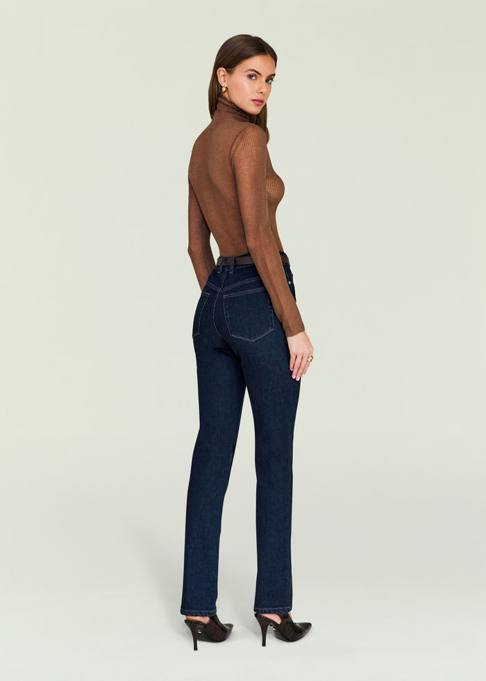 Side view of a woman wearing a brown ribbed turtleneck Piper Top with dark jeans.