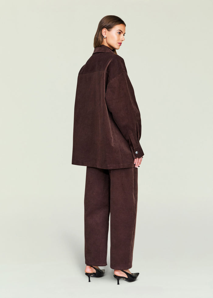 Three quarter view of a brown corduroy shacket over a brown turtleneck, belted at the waist with wide leg pants.