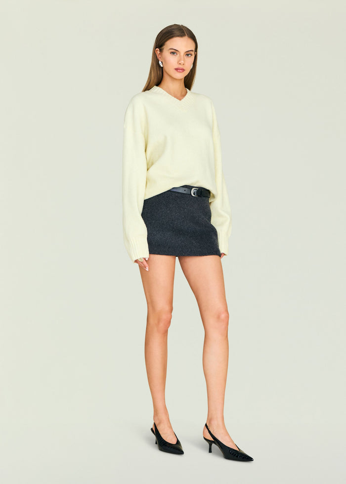 Model in cream Alejandra Sweater tucked into a dark mini skirt with a black belt and black heels.