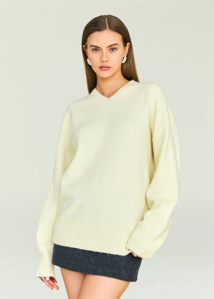 Model wearing cream Alejandra Sweater with a relaxed fit and V neckline, accessorized with silver earrings.