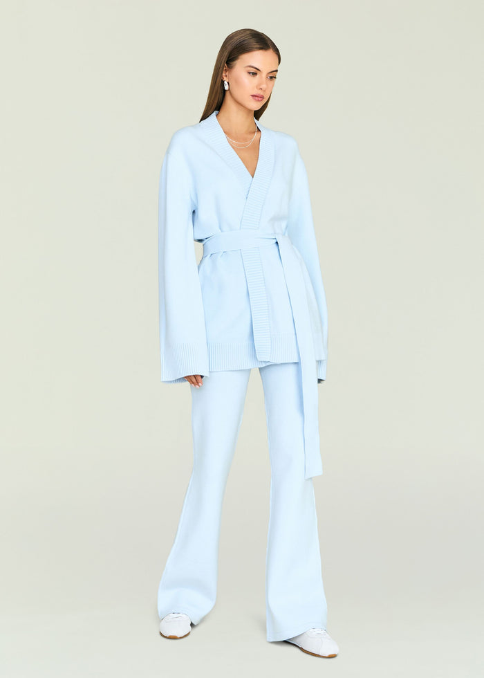 Model in pale blue knit belted cardigan and matching pants with white sneakers.