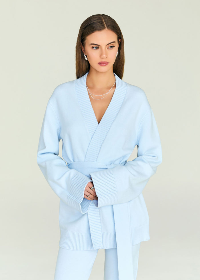 Model in a light blue cardigan with a deep V wrap neckline and belt, styled with silver jewelry.