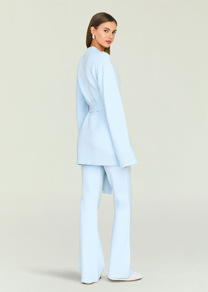 Back view of a model wearing a pale blue knit cardigan with belt and matching pants.
