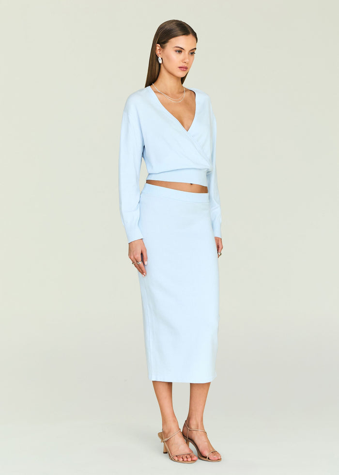 Model in pale blue knit wrap top and matching midi skirt with wrap detail and exposed midriff