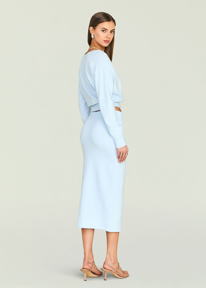 Side view of a model in a pale blue reversible knit top and matching pencil skirt with a waist cutout and strappy sandals.