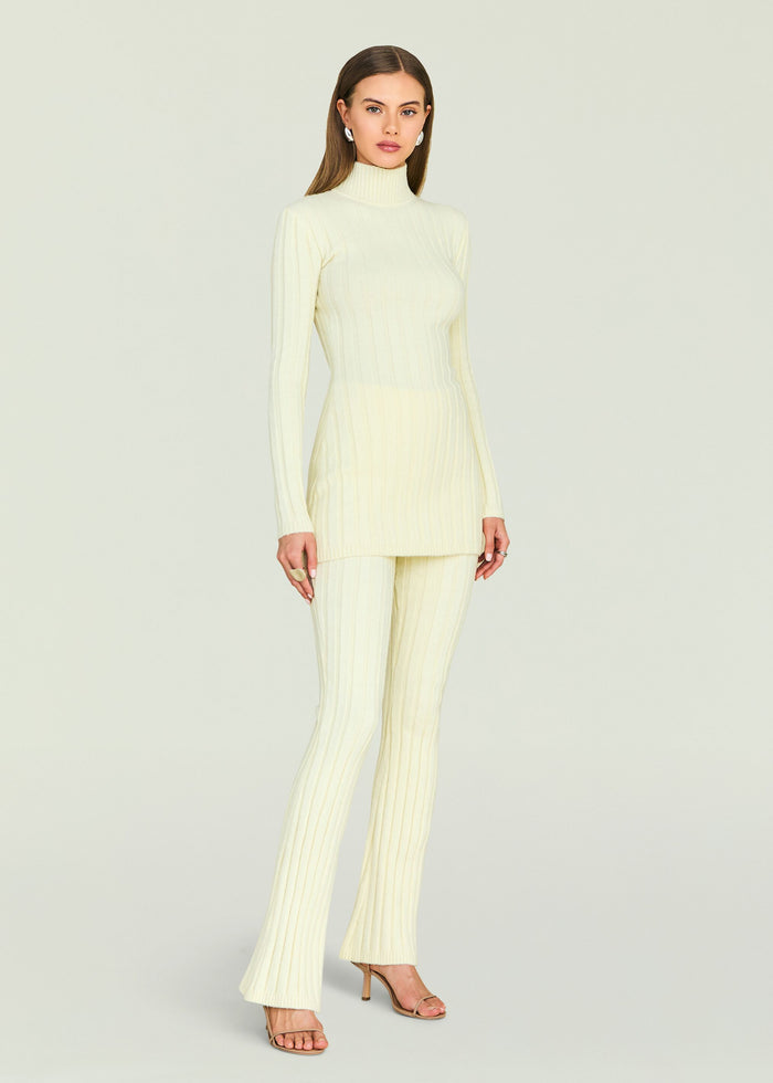 Ivory ribbed knit turtleneck tunic with matching pants on a model wearing strappy heels.