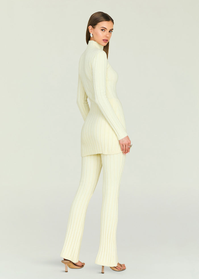 Side view of a model wearing a cream Velira knit top and matching ribbed pants.