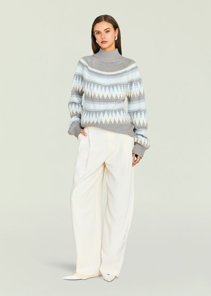 Front view of a model in a grey blue geometric Tirza sweater paired with white pants