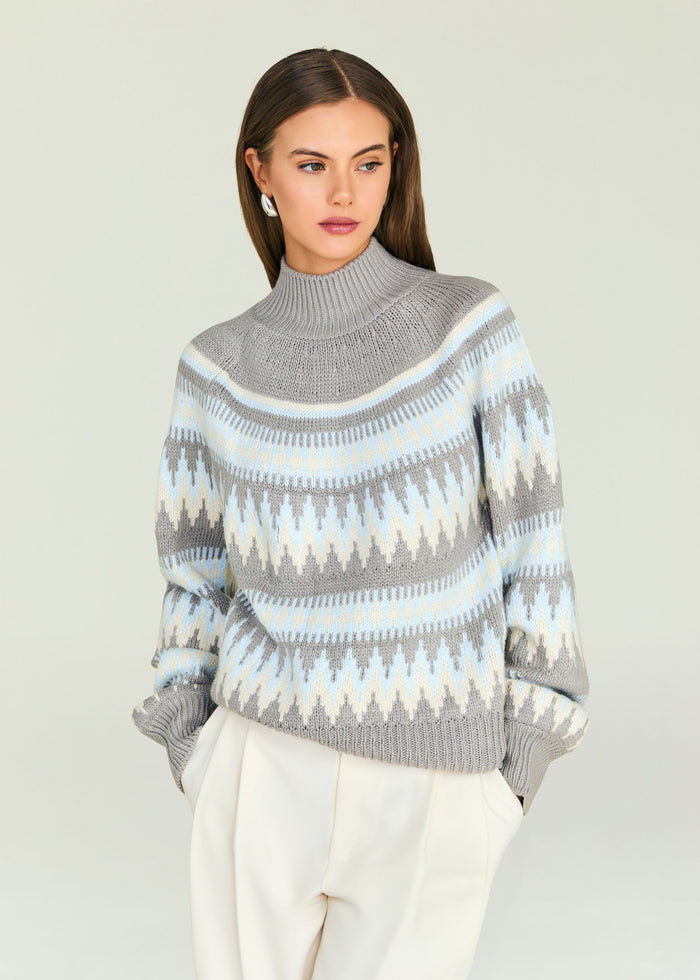 Model wearing a gray patterned knit turtleneck sweater with light blue and white bands