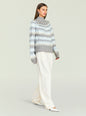 Model in a gray patterned knit turtleneck sweater with light blue and white bands paired with white trousers thumbnail image 3 of 5