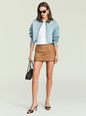 Model wearing a light wash denim jacket with a brown collar over a white top and tan mini skirt, with a black handbag and sunglasses thumbnail image 2 of 5