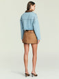 Back view of cropped light denim Coop Jacket with brown leather collar over a white top and tan skirt. thumbnail image 5 of 5