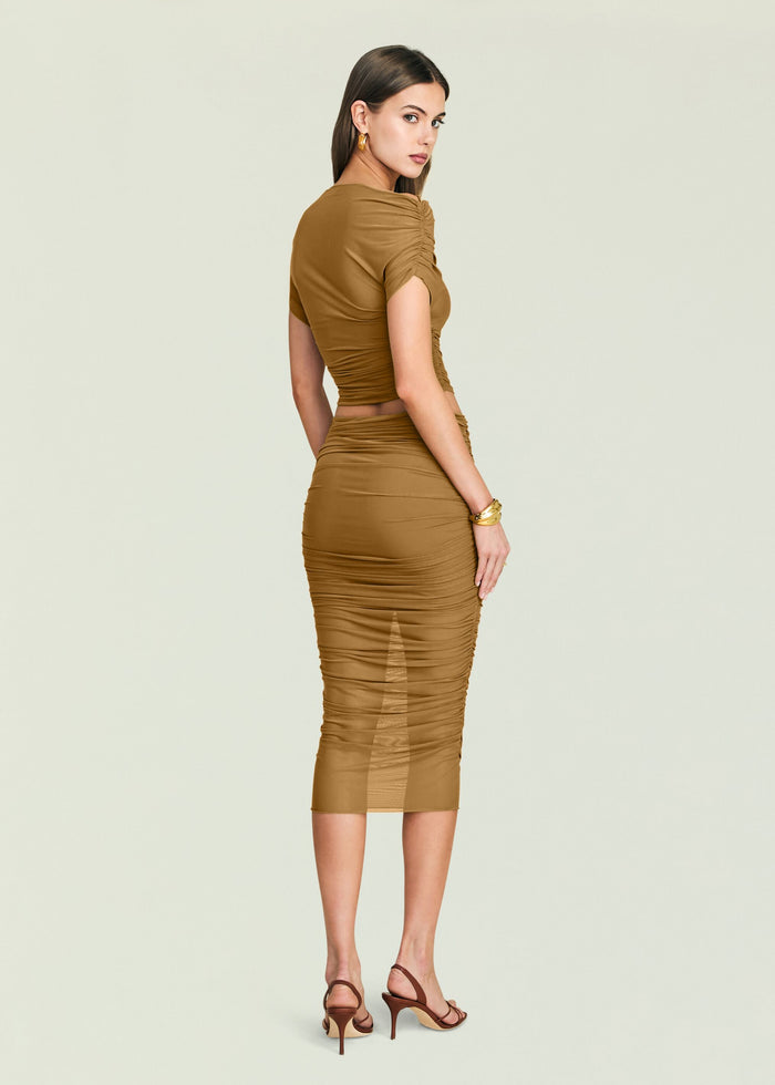 Back view of a model in a tan Marsh Top ruched crop top and matching skirt, holding a dark clutch.